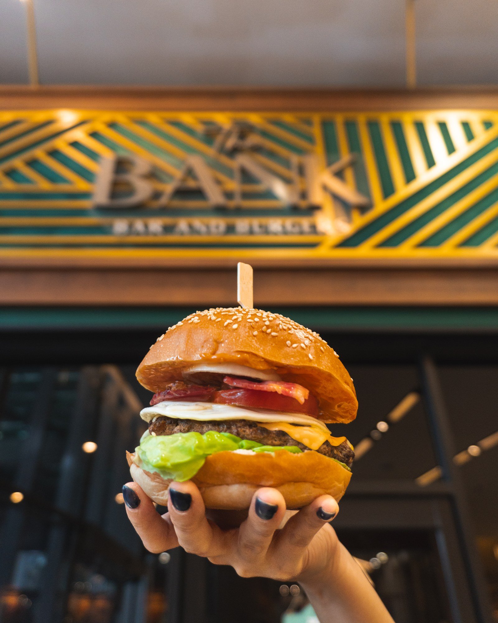 Burger held up in front of The Bank Bar and Burgers sign
